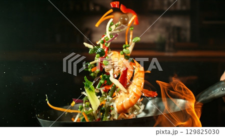 Freeze Motion of Wok Pan with Flying Ingredients in the Air and Fire Flames. Kitchen Interior on Background. 129825030