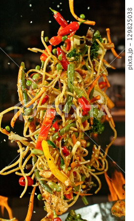 Freeze Motion of Wok Pan with Flying Ingredients in the Air and Fire Flames. Kitchen Interior on Background. Vertical Aspect Ratio. 129825038