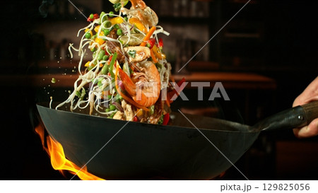 Freeze Motion of Wok Pan with Flying Ingredients in the Air and Fire Flames. Kitchen Interior on Background. 129825056