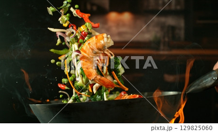 Freeze Motion of Wok Pan with Flying Ingredients in the Air and Fire Flames. Kitchen Interior on Background. 129825060