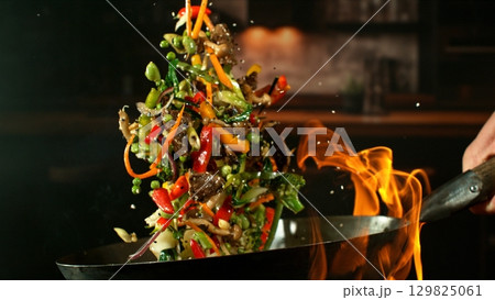 Freeze Motion of Wok Pan with Flying Ingredients in the Air and Fire Flames. Kitchen Interior on Background. 129825061