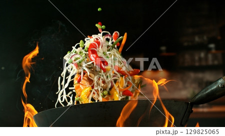 Freeze Motion of Wok Pan with Flying Ingredients in the Air and Fire Flames. Kitchen Interior on Background. Freeze Motion of Wok Pan with Flying Ingredients in the Air and Fire Flames. Kitchen Interior on Background. 129825065