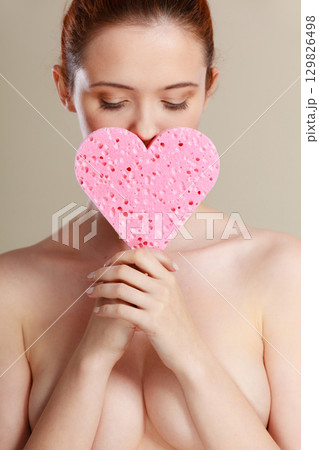 Naked woman holding pink heart sponge in hands. 129826498