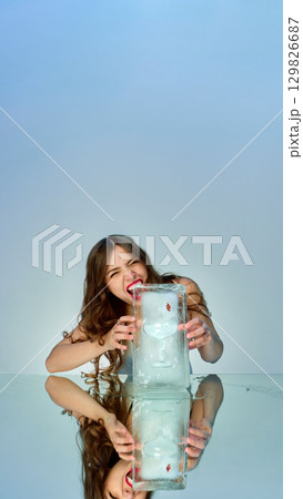 Young woman biting ice block with frozen cocktail inside showing playful expression 129826687