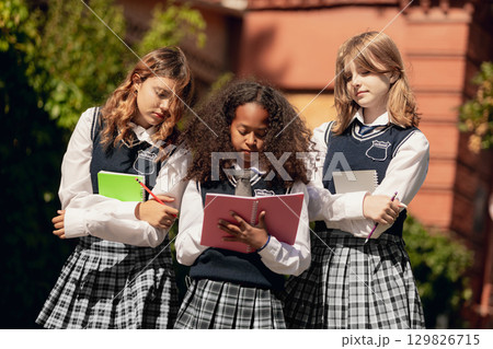 Diverse schoolgirls in uniforms discussing notes with teamwork spirit Diverse schoolgirls in uniforms discussing notes with teamwork spirit 129826715