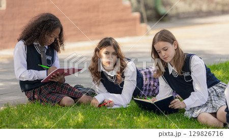 Teen girls in school uniforms reading and writing with serious expressions Teen girls in school uniforms reading and writing with serious expressions 129826716