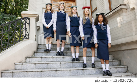 Teenage girls in school uniform standing on stairs with books on heads showing discipline Teenage girls in school uniform standing on stairs with books on heads showing discipline 129826726