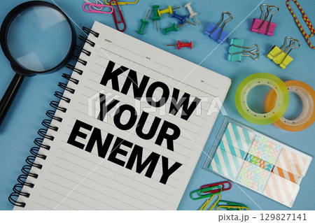 Know Your Enemy text with magnifying glass on blue background 129827141