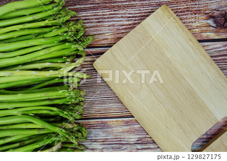 Bunch of fresh green asparagus stems with cutting wooden board on wooden background 129827175