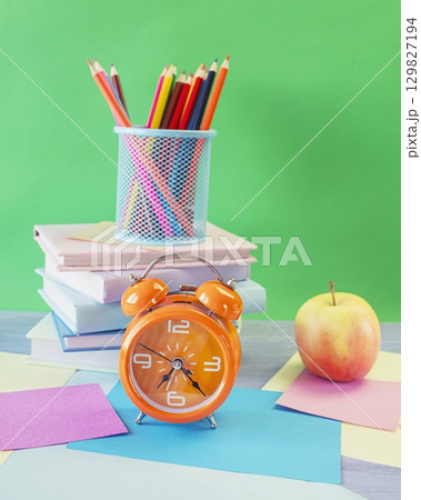 Back to school concept. Alarm clock, stack of books, apple, colored pencils and pastel colored paper on bright background. 129827194