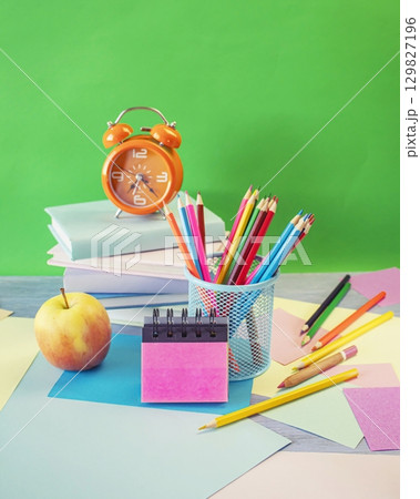 Back to school concept. Alarm clock, stack of books, apple, colored pencils and pastel colored paper on bright background. Back to school concept. Alarm clock, stack of books, apple, colored pencils and pastel colored paper on bright background. 129827196