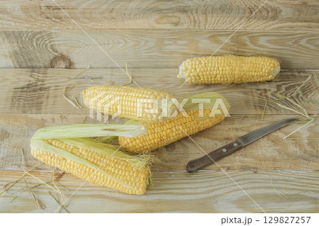 Fresh corn on the cob on a cutting board with a knife on a wooden background, fresh vegetables, healthy food. 129827257