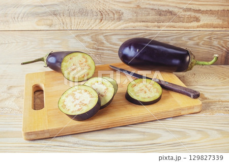 Fresh eggplants on cutting board and knife on wooden background, cooking fresh vegetables in kitchen, healthy food. 129827339