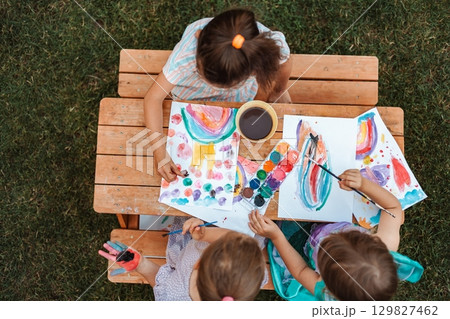Children painting with watercolors at a wooden table in a garden 129827462