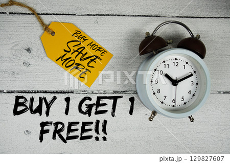 Buy 1 Get 1 Free!! Buy More Save More with price tag and alarm clock on wooden background 129827607