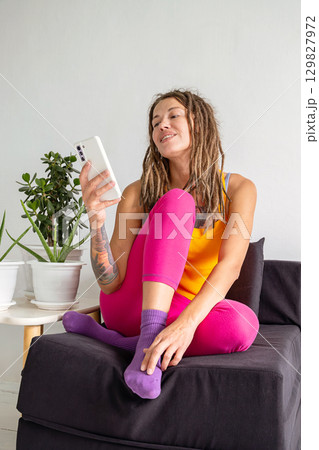 Woman with dreadlocks relaxing on a sofa while holding a mobile phone. 129827972