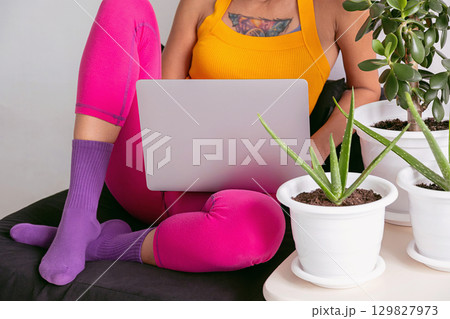 Woman in colorful clothes working on laptop at home office, surrounded by green plants 129827973