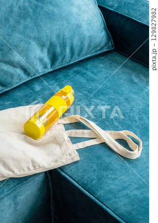 Yellow water bottle and white eco bag on blue sofa. Yellow water bottle and white eco bag on blue sofa. 129827982