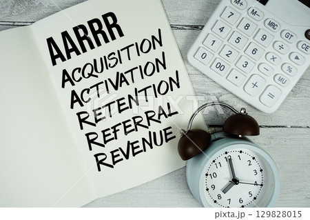AARRR Acquisition, Activation, Retention, Referral, Revenue text on paper notebook page with alarm clock and calculator on wooden background 129828015