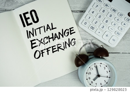 IEO Initial Exchange Offering text on paper notebook page with alarm clock and calculator on wooden background IEO Initial Exchange Offering text on paper notebook page with alarm clock and calculator on wooden background 129828023