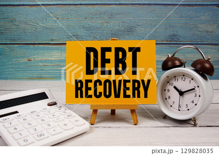 Debt Recovery text written on paper card with calculator and alarm clock on wooden background Debt Recovery text written on paper card with calculator and alarm clock on wooden background 129828035