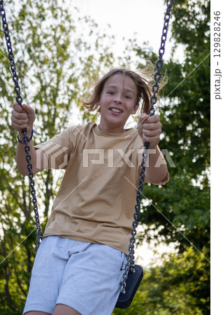 Carefree boy enjoying playing on swing in playground during summer holidays, having fun outdoors 129828246