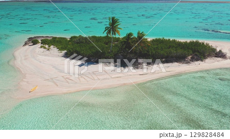 Crystal clear turquoise waters surround a small sandy island featuring lush greenery and a palm tree. The word 'TRAVEL' is written in the sand, inviting exploration and adventure. Crystal clear turquoise waters surround a small sandy island featuring lush greenery and a palm tree. The word 'TRAVEL' is written in the sand, inviting exploration and adventure. 129828484