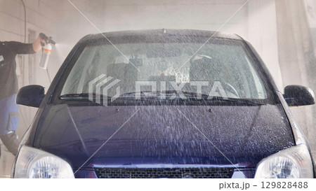 Car wash worker cleaning vehicle with pressurized water jet 129828488