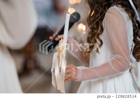 Young Flower Girl Holding Lit Candle at Orthodox Christian Wedding Ceremony, White Lace Dress, Soft Lighting Young Flower Girl Holding Lit Candle at Orthodox Christian Wedding Ceremony, White Lace Dress, Soft Lighting 129828514