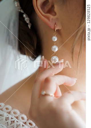 Elegant Bride Holding Pearl Earrings: Close-up Wedding Jewelry Shot, Soft White Lace, Delicate Pearls, Golden Metal, Romantic and Luxurious Style. Elegant Bride Holding Pearl Earrings: Close-up Wedding Jewelry Shot, Soft White Lace, Delicate Pearls, Golden Metal, Romantic and Luxurious Style. 129828525