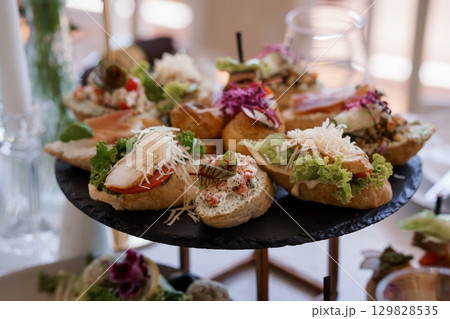Elegant Catering Display with Salmon Canapes on Slate Tiered Tray, Wedding Reception Appetizers, Gourmet Food Presentation, Dark Background Elegant Catering Display with Salmon Canapes on Slate Tiered Tray, Wedding Reception Appetizers, Gourmet Food Presentation, Dark Background 129828535