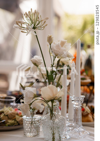 Elegant Wedding Table Setting with White Flowers, Candles, and Crystal Vases: Romantic Dinner Reception, Fine Dining, Luxurious Decor. 129828545