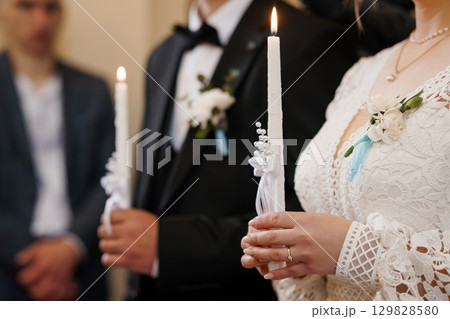 Orthodox Wedding Candle Lighting Ceremony: Groom and Bride Holding Lit Candles in Lace Gown, Dark Suit, Spiritual Ritual. 129828580
