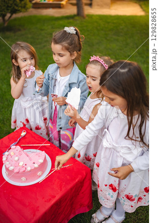 Young girls share joyful moments around a cake outdoors. Young girls share joyful moments around a cake outdoors. 129828655