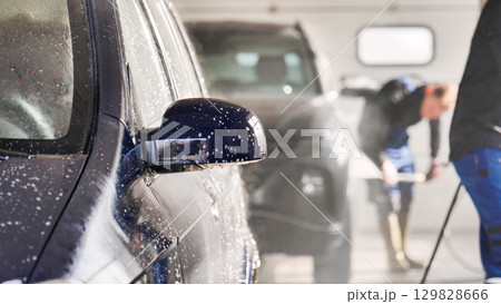 Car wash workers cleaning vehicle with high pressure water jet 129828666
