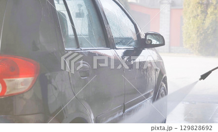 Worker washing car with high pressure water jet in car wash 129828692