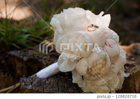 Wedding Rings on Peony Bouquet - Romantic Marriage Ceremony Symbolism with White Flowers, Gold Bands, Natural Forest Backdrop, Soft Focus Style Wedding Rings on Peony Bouquet - Romantic Marriage Ceremony Symbolism with White Flowers, Gold Bands, Natural Forest Backdrop, Soft Focus Style 129828710
