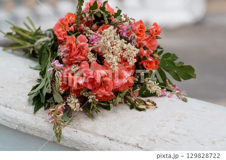 Coral Wedding Bouquet with Rings on Stone Ledge, Romantic Flowers, Celebration, Peach Tones, Bridal Arrangement, Outdoor Ceremony Detail. Coral Wedding Bouquet with Rings on Stone Ledge, Romantic Flowers, Celebration, Peach Tones, Bridal Arrangement, Outdoor Ceremony Detail. 129828722