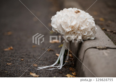 Wedding Rings on White Bouquet Resting by Curb. Romantic Scene, Soft Focus, Floral, Asphalt, Gold, Marriage, Love, Commitment, Ceremony 129828755