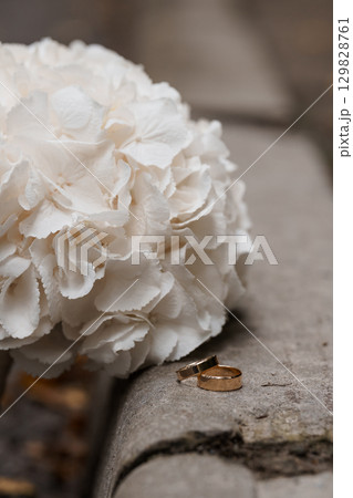 Wedding Rings on Hydrangea: Symbolic Gold Bands Resting Near White Flowers, Elegant Stone Surface, Romantic Celebration. Wedding Rings on Hydrangea: Symbolic Gold Bands Resting Near White Flowers, Elegant Stone Surface, Romantic Celebration. 129828761