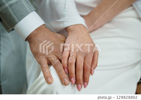 Wedding Rings Exchange Ceremony Close-Up: Gold Bands on Hands of Bride and Groom, White Attire, Celebrating Love and Commitment. Wedding Rings Exchange Ceremony Close-Up: Gold Bands on Hands of Bride and Groom, White Attire, Celebrating Love and Commitment. 129828802