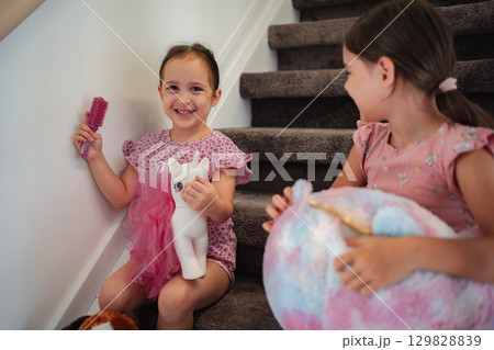 Two happy little sisters playing with their toys on the stairs at home Two happy little sisters playing with their toys on the stairs at home 129828839