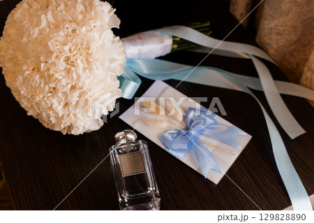 Wedding Preparations Still Life: Bouquet, Perfume, and Invitation in Light Blue and Cream Tones, Elegant Bridal Accessories on Dark Wood Surface. 129828890