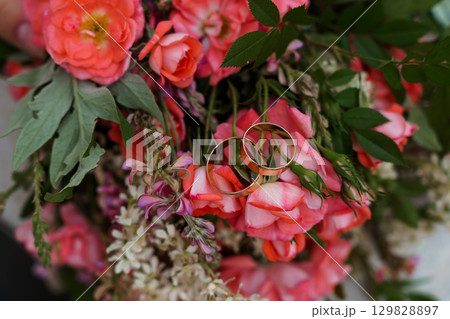 Wedding Rings Amongst Coral Roses: Close-up of Golden Bands Symbolizing Love and Commitment in Vibrant Floral Arrangement Wedding Rings Amongst Coral Roses: Close-up of Golden Bands Symbolizing Love and Commitment in Vibrant Floral Arrangement 129828897