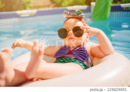 Cute Mermaid Baby Girl in Sunglasses Relaxing on Float in Pool on Sunny Day 129829891