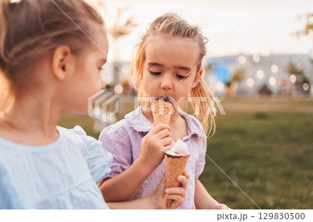 Two little girls are eating ice cream cones in a park 129830500