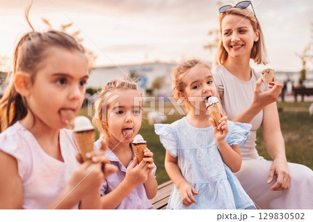 Mother and daughters enjoying ice cream cones in a park Mother and daughters enjoying ice cream cones in a park 129830502