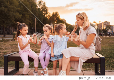Mother and daughters enjoying ice cream cones in a park at sunset Mother and daughters enjoying ice cream cones in a park at sunset 129830506