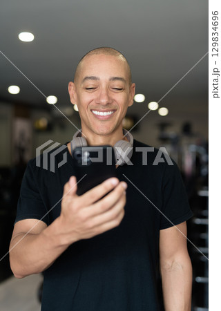 Hispanic bald man athlete in gym using mobile phone Hispanic bald man athlete in gym using mobile phone 129834696