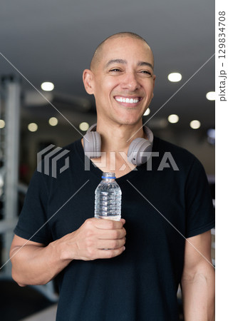 Hispanic bald man athlete in gym drinking water from bottle 129834708